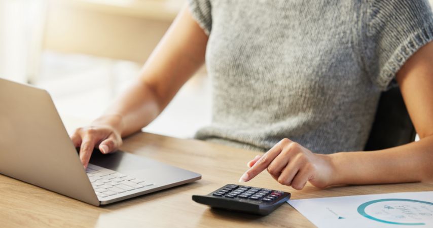 Mulher usando o notebook e a calculadora ao mesmo tempo.