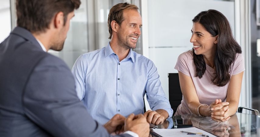 Uma mulher e dois homens com roupas sociais, em um ambiente empresarial, com semblante de satisfação e documentos em cima da mesa.