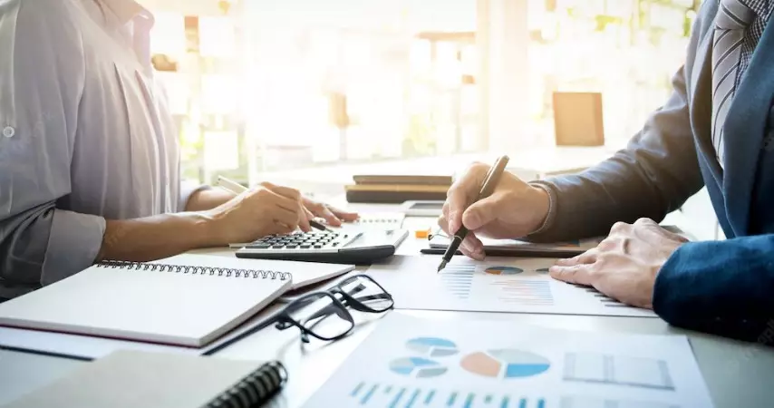 Dois homens analisando vários gráficos em uma mesa de escritório. 