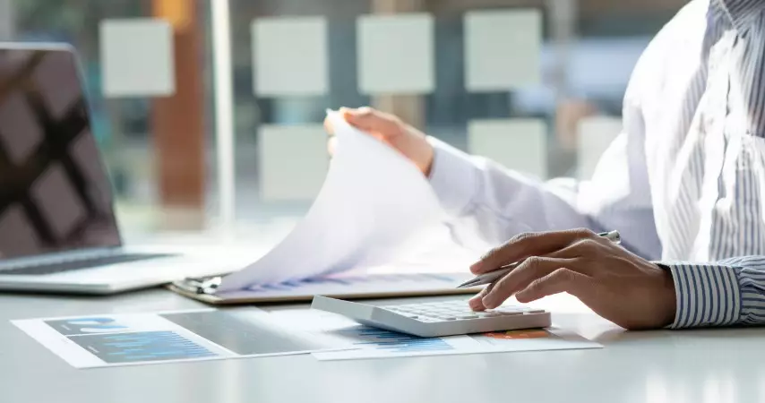 Homem analisando documentos e calculando em uma calculadora 