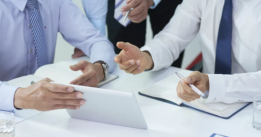 Homens reunidos em uma mesa analisando a tela de um tablet e discutindo sobre a LGPD para empresas.